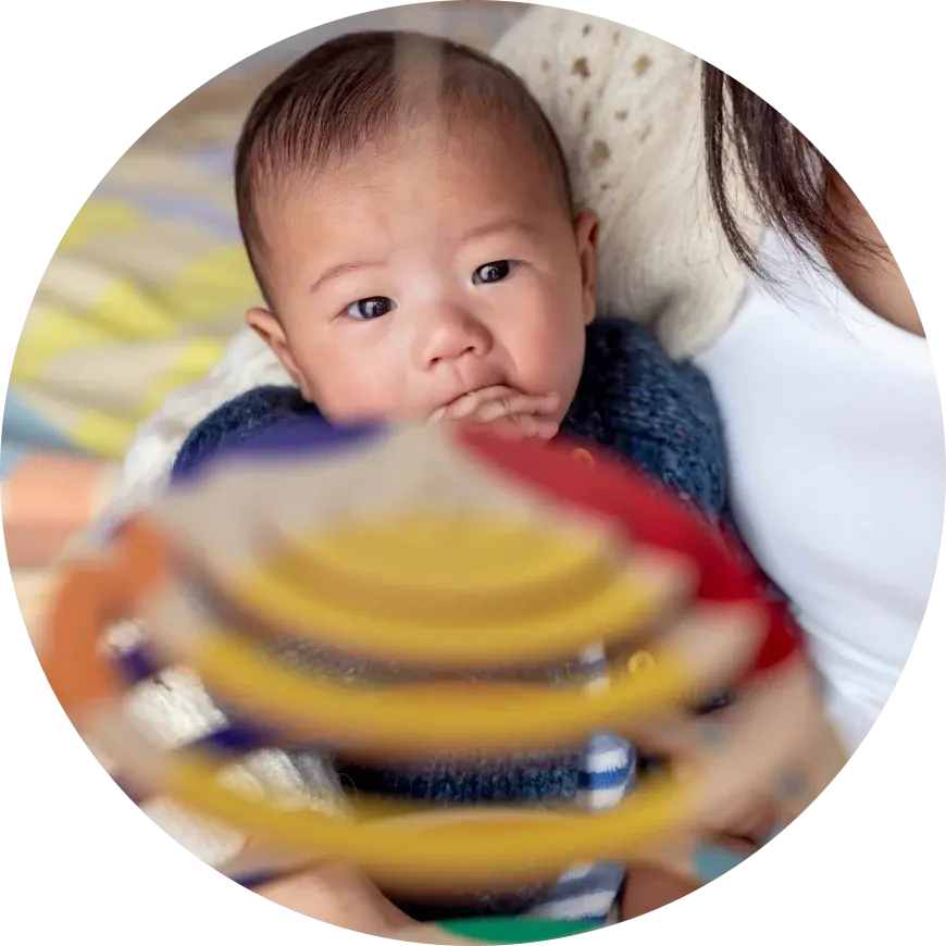 怀抱中的宝宝正玩着彩虹叠叠乐 / A baby in a caregiver's arms playing with a rainbow stacker